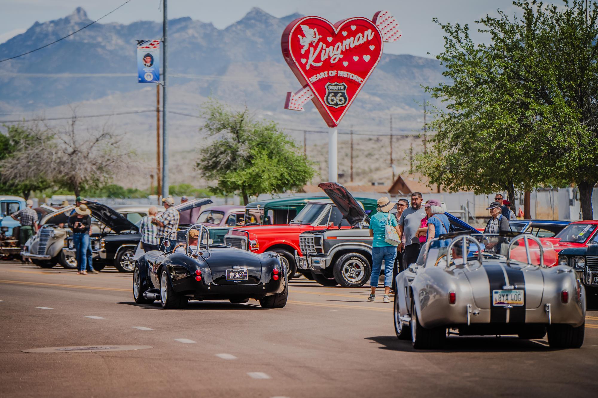 Classic cars line Route 66 in Kingman, AZ. Mountains in the background and a heart shaped neon sign that reads 