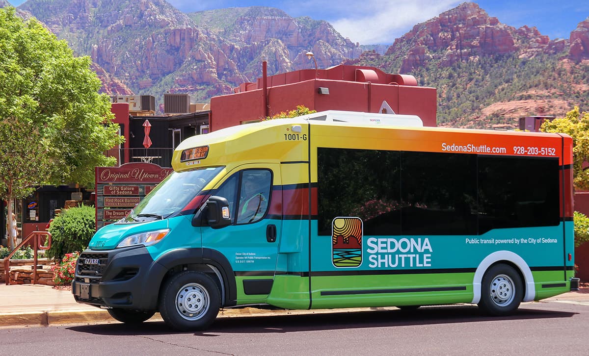 Sedona Shuttle on city street in front of businesses and rock formations in background
