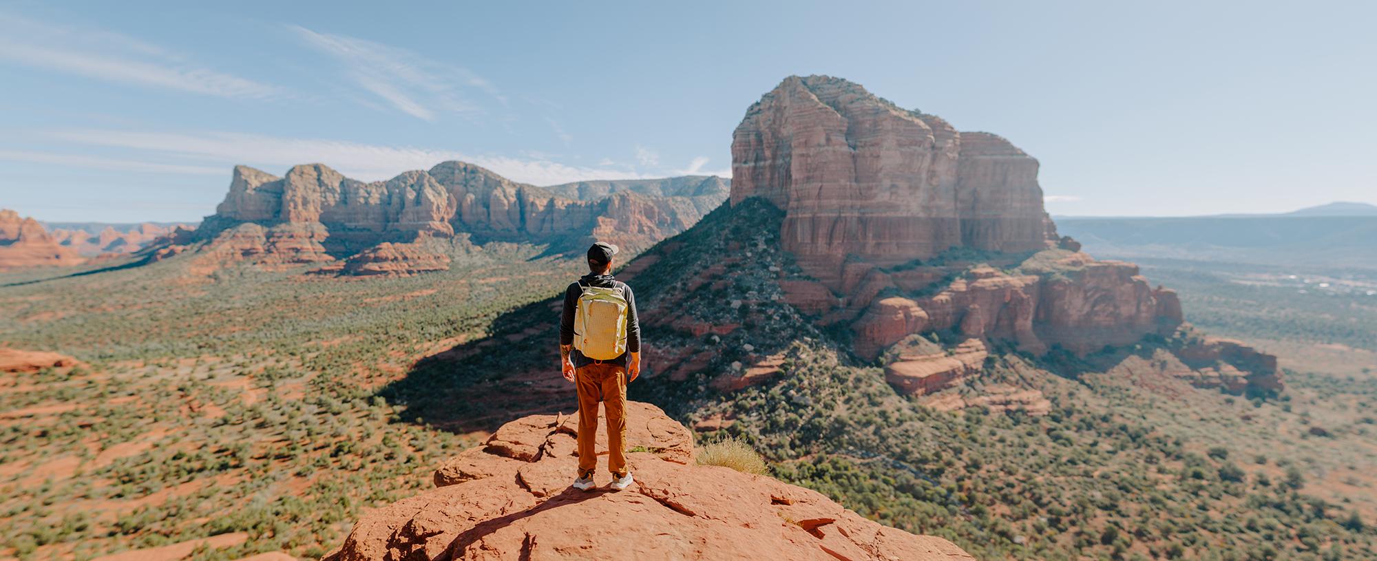 A man stands on top of a Sedona red rock formation looking at the horizon